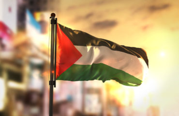 Palestine Flag Against City Blurred Background At Sunrise Backlight