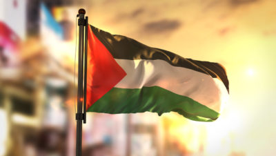 Palestine Flag Against City Blurred Background At Sunrise Backlight
